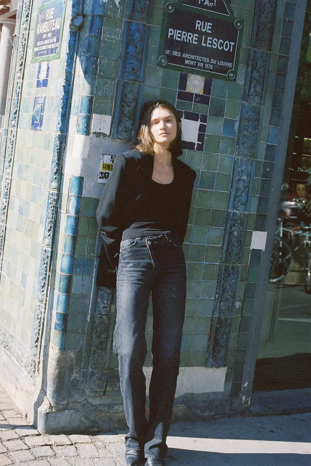 Full-length portrait in black beside a blue-tiled street corner.