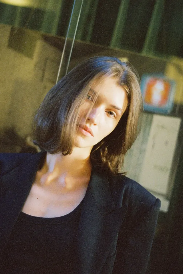 Close portrait with a short bob, black jacket and warm sunlight.