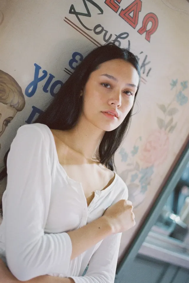 Portrait in a white blouse against a painted shop wall.