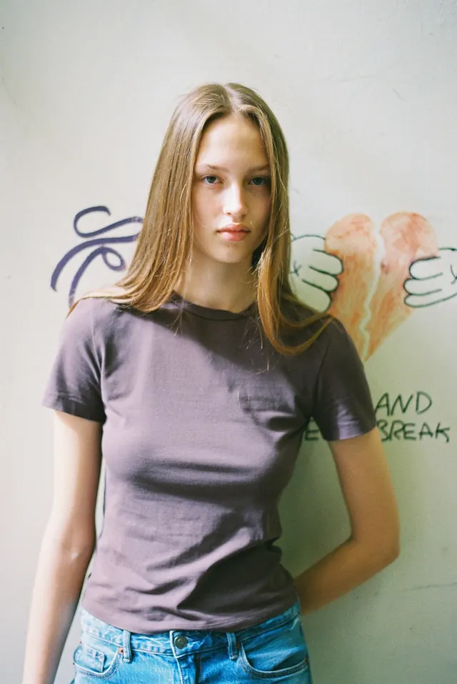 Portrait in a grey T-shirt and jeans against a pale illustrated wall.