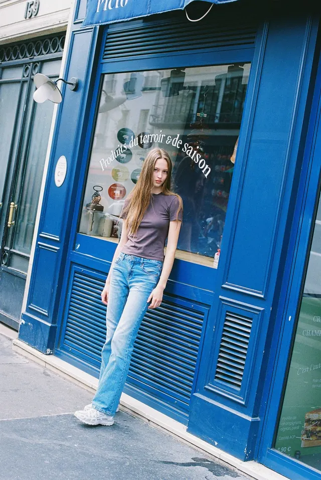 Full-length portrait in jeans outside a vivid blue shopfront.