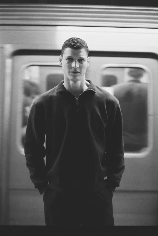 Black-and-white portrait in a dark sweater before a passing train.