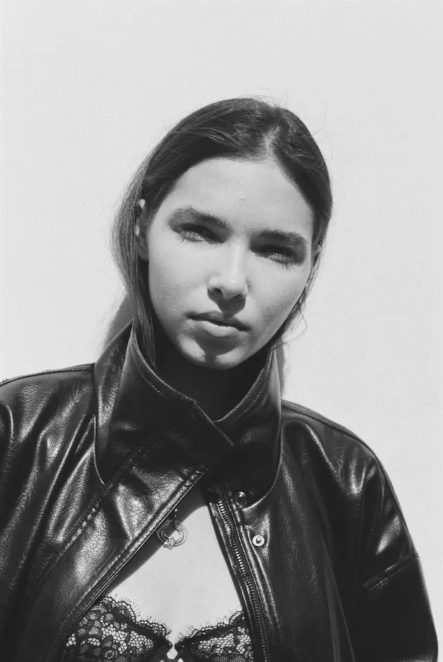Black-and-white close portrait in a leather jacket against a pale sky.