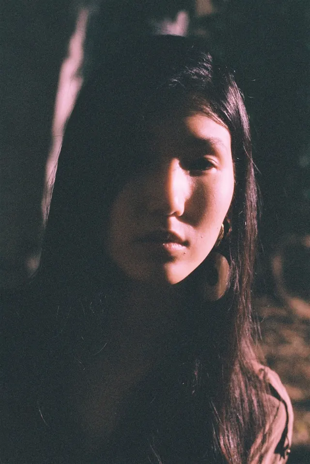 Close portrait with one side of the face caught in pink light.
