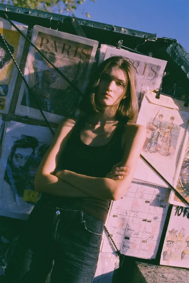 Portrait in a black vest and jeans among prints at a riverside stall.