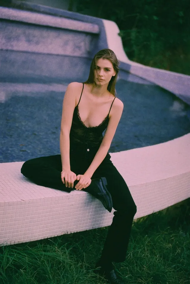 Seated portrait in a black dress on a curved pale bench.