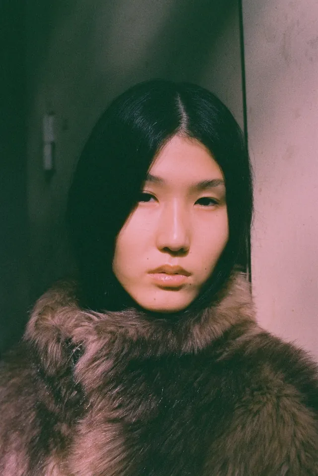 Close portrait framed by a textured coat and a softly lit doorway.