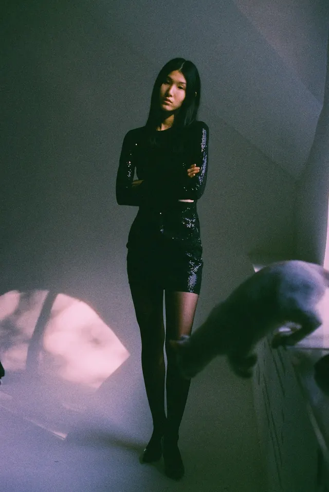 Full-length portrait in a black dress in a studio with a pink pool of light.