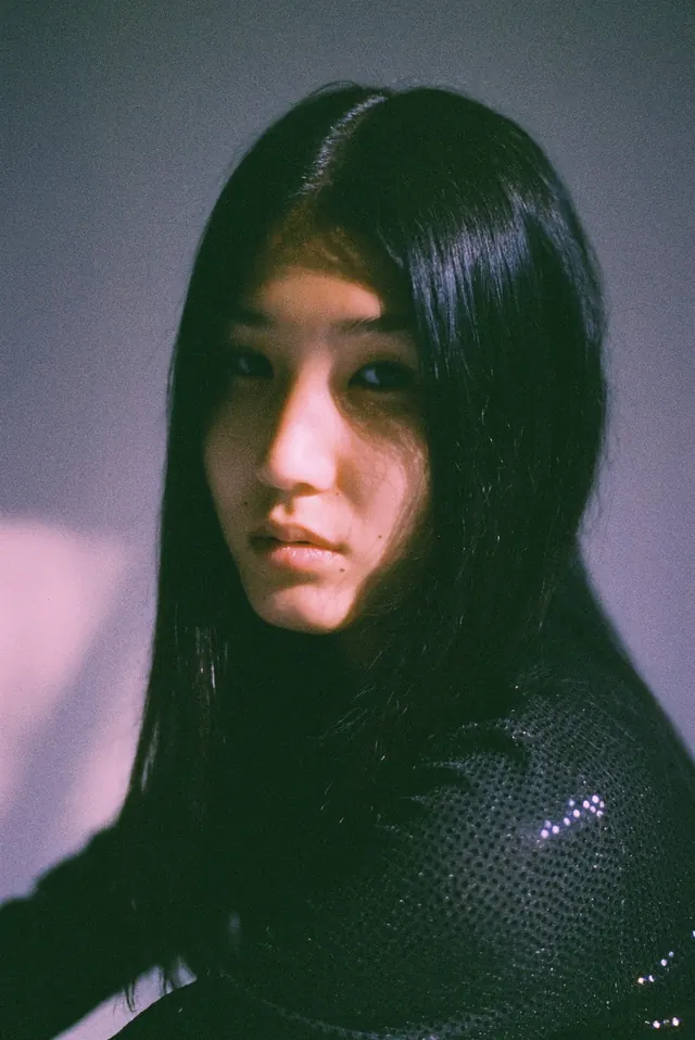 Close portrait in a black dress against lilac light and deep shadow.