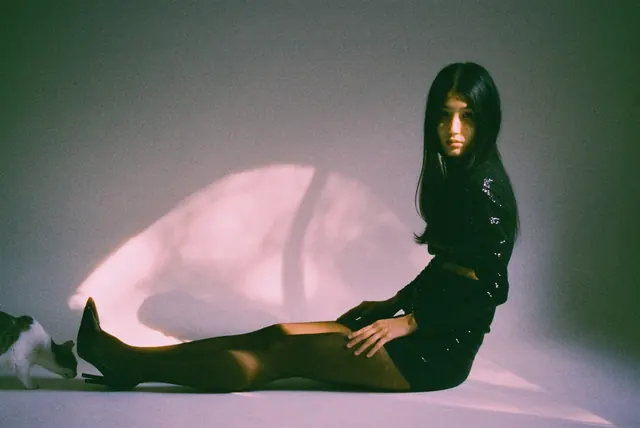 Horizontal seated studio portrait in black with an oval patch of pink light.