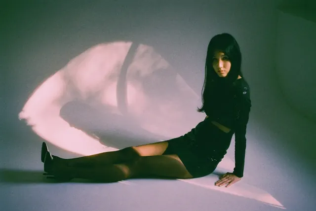 Horizontal seated studio portrait in black, with an oval of pink light and cast shadows.